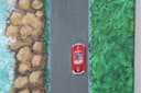 A bird's eye view of the coast, with a red Porsche on the road